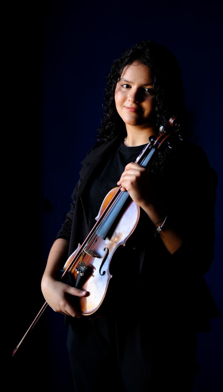 Aluna do Projeto Aldo Parisot segura seu violino e sorri