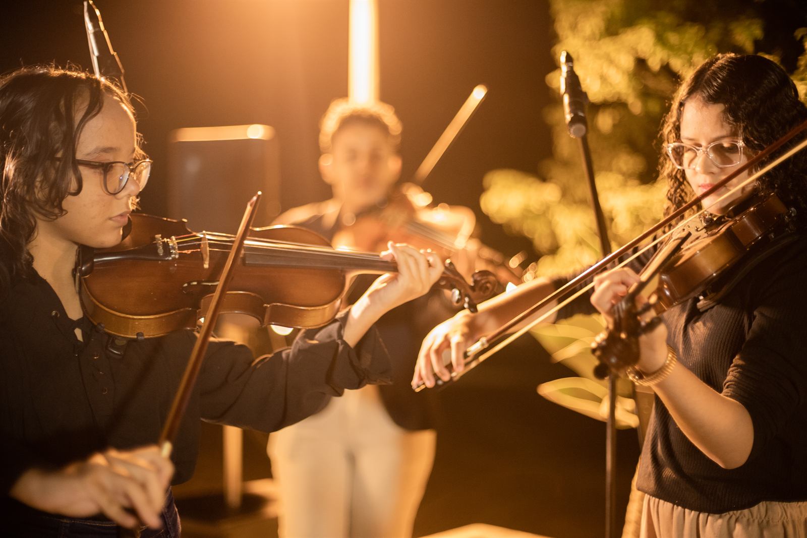 Duas alunas tocam violino sob luz quente durante apresentação