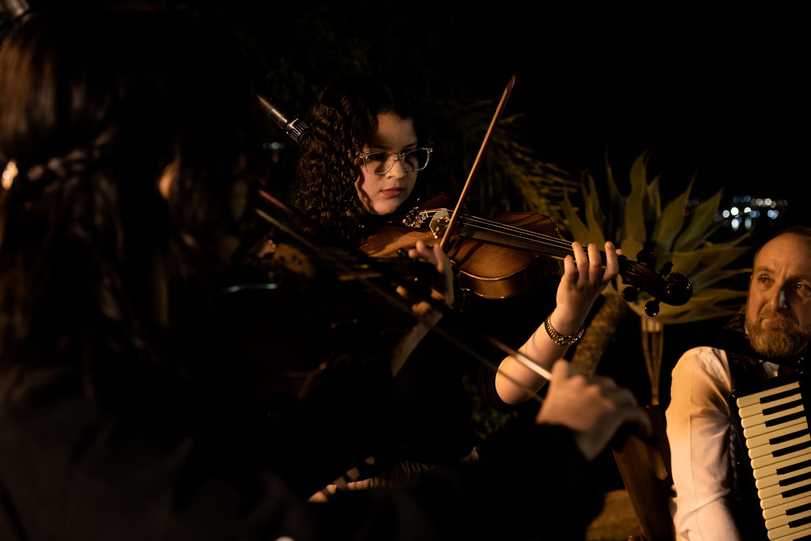 Menina tocando violino no recital beneficente em Brasília — close emocional com iluminação dourada